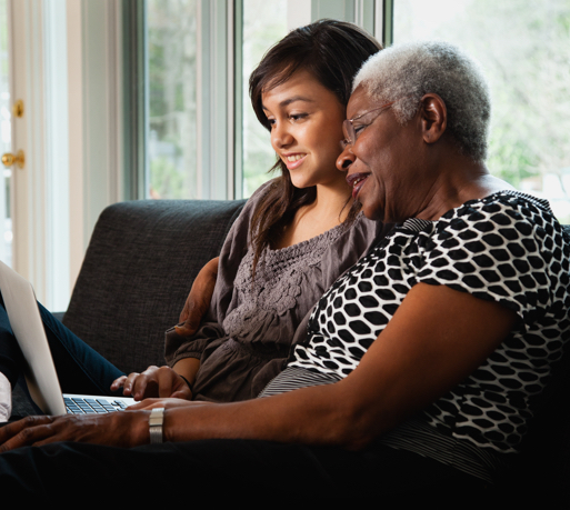 A teen helps an elderly woman on her laptop.